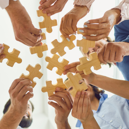 un groupe de personnes en cercle vue d'en bas ayant chacune une pièce de puzzle dans la main